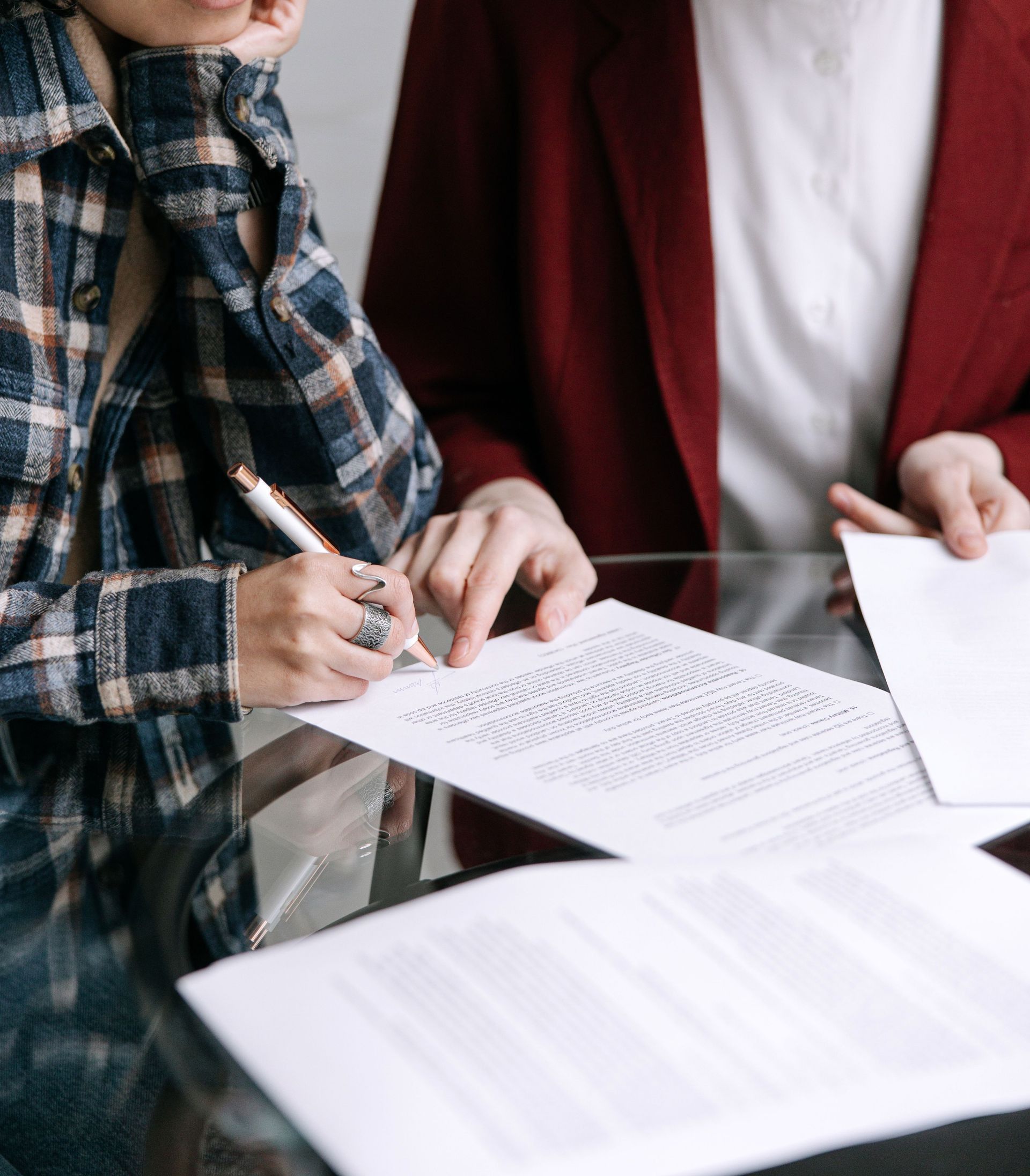 Two women reviewing and signing documents together at a glass table indoors.